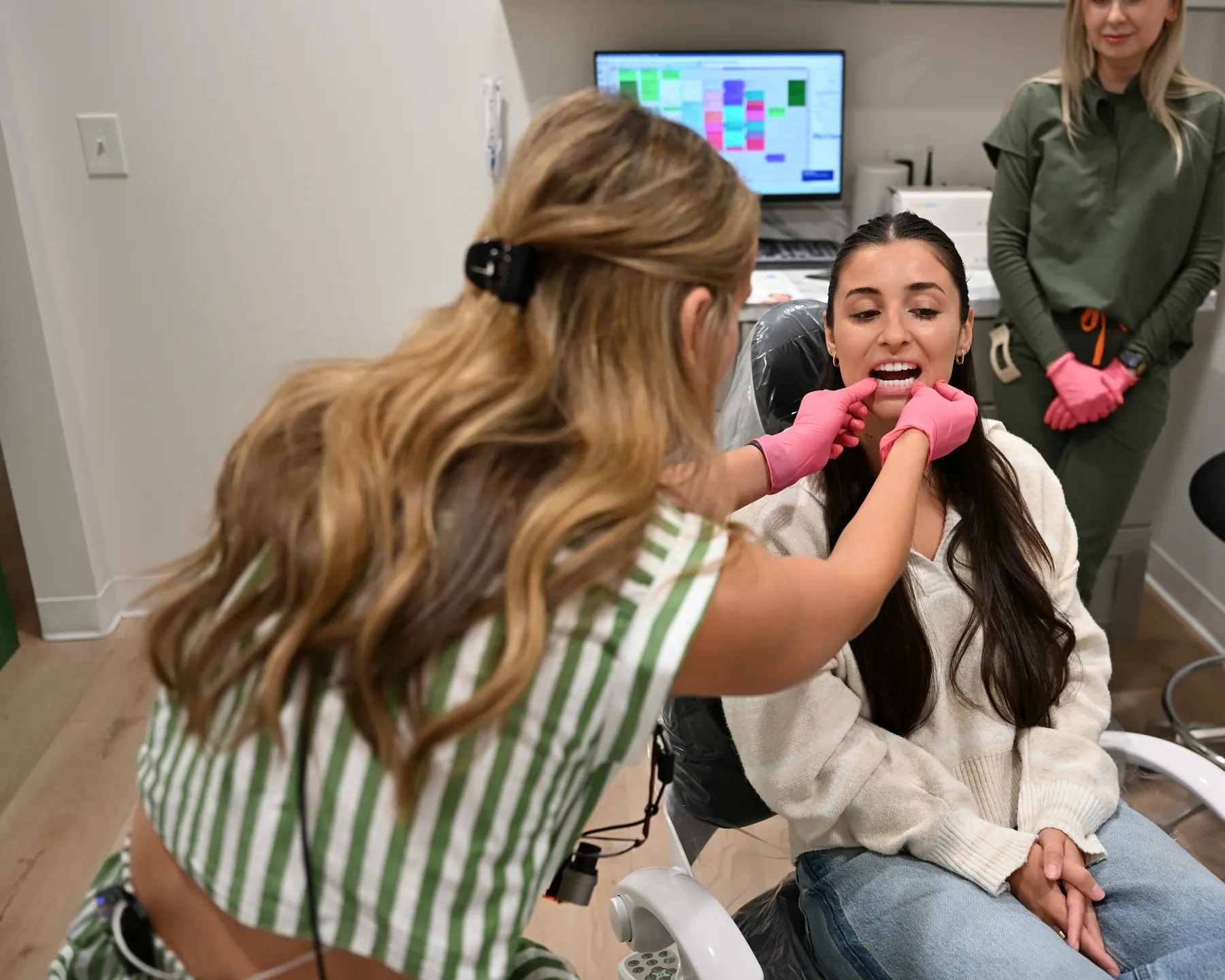 A clinician examining a patient in the chair while a team member looks on