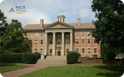 Historic brick building with columns, surrounded by trees and greenery. It has a domed cupola on the roof and a wide staircase entrance.