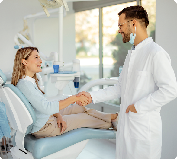 A person in a dental chair shakes hands with a dentist in an office equipped with modern dental instruments.