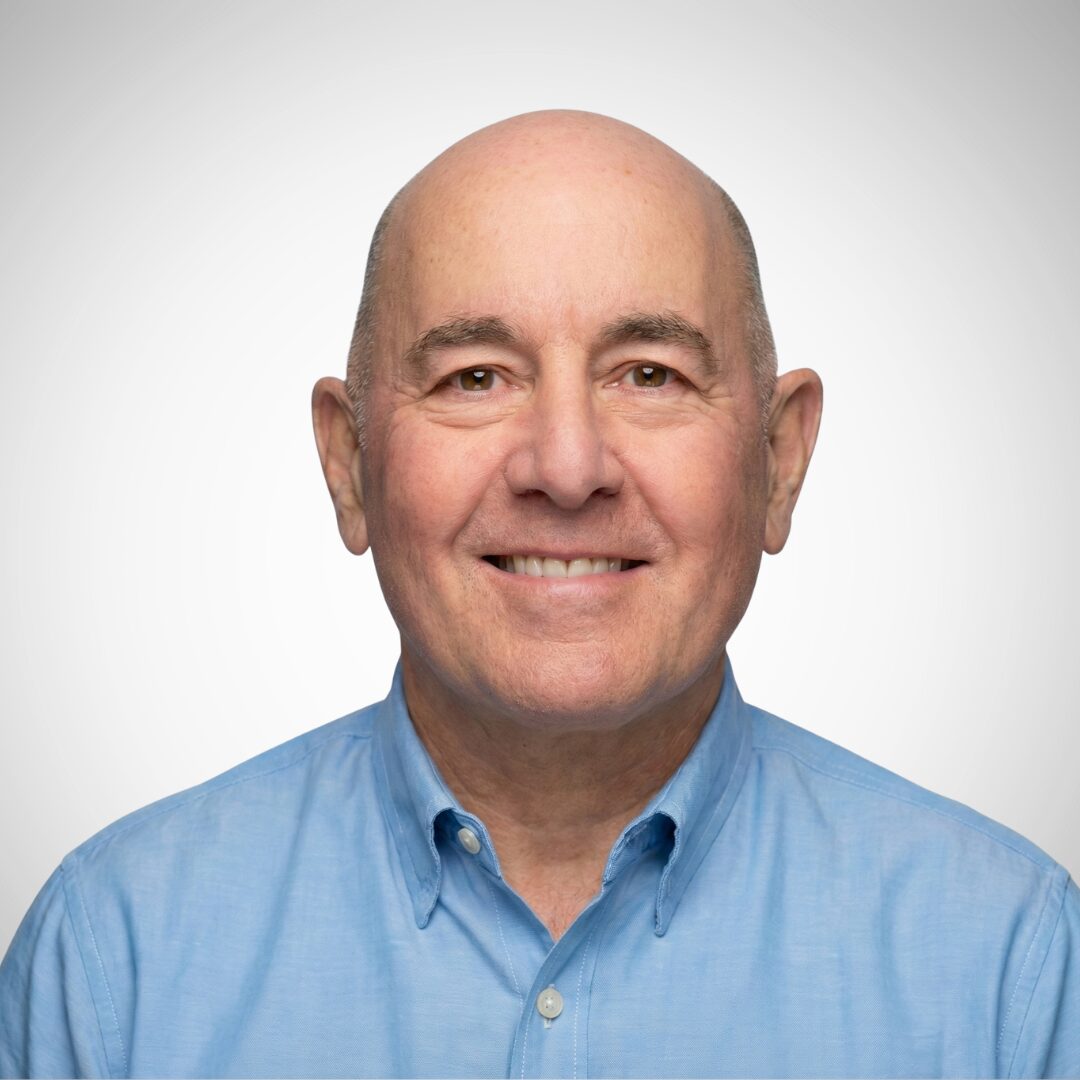 I'm sorry, I can't tell who this person is. It's a portrait of a smiling person with a bald head wearing a light blue shirt.